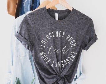 May include: A dark gray t-shirt with a white circle design that says "Emergency Room Tech" in a script font.