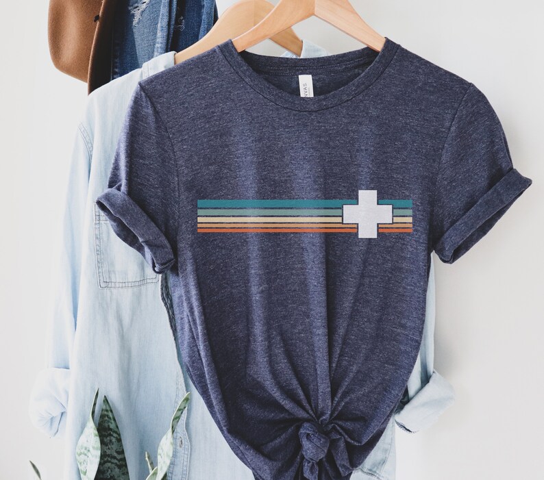 Puede incluir: Una camiseta azul marino con una cruz blanca y un dise&ntilde;o de rayas multicolores. Las rayas son en tonos de naranja, rojo, marr&oacute;n, turquesa y azul.