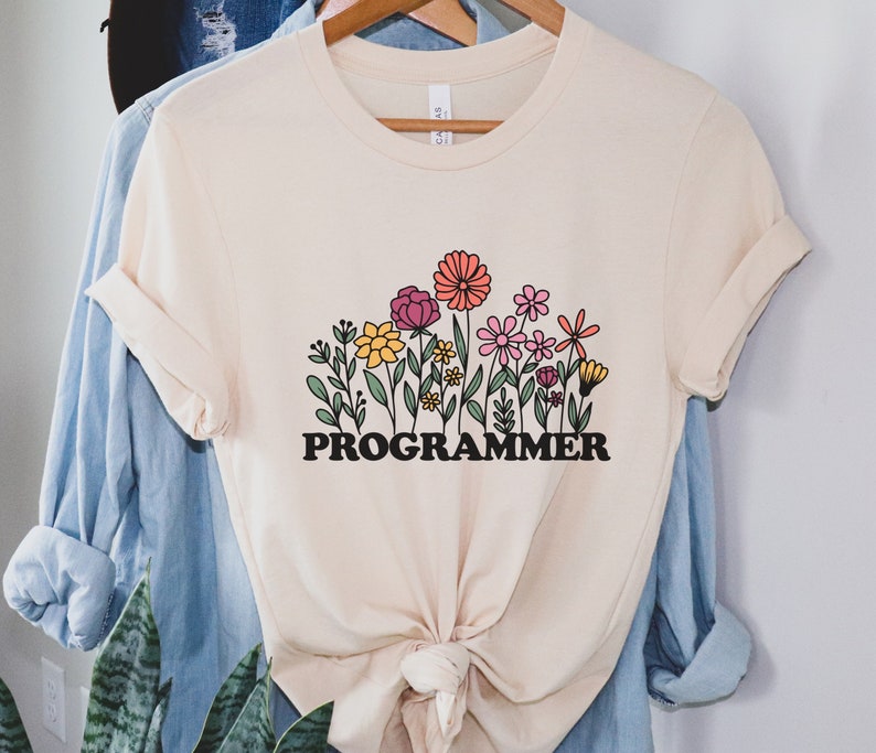 May include: A cream colored t-shirt with a graphic of colorful flowers and the word "PROGRAMMER" in black letters.