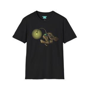 May include: Black t-shirt with a detailed illustration of an anglerfish. The design features a glowing lure, skeletal structure, and sharp teeth, in gold and green. The shirt has a crew neck and short sleeves.