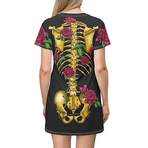 May include: Black dress featuring a golden skeleton design with red roses and green leaves. The dress has short sleeves and a scoop neckline. The skeleton design is centered on the back of the dress.