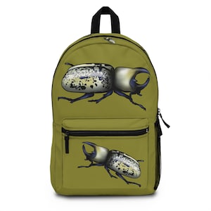 May include: Olive green backpack featuring a large illustration of a beetle with a white and black speckled shell and a large horn. The backpack has a black zipper, a front pocket, and a side mesh pocket.