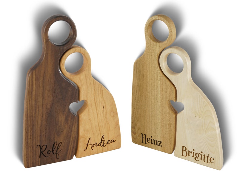 May include: Two wooden cutting boards shaped like people, with a heart cutout where they touch. The boards are personalized with the names "Rolf", "Andrea", "Heinz", and "Brigitte".
