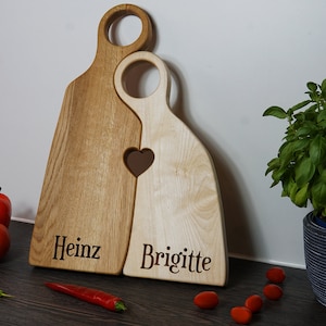 May include: Two wooden cutting boards shaped like people, with a heart cutout where they touch. The boards are engraved with the names "Heinz" and "Brigitte".