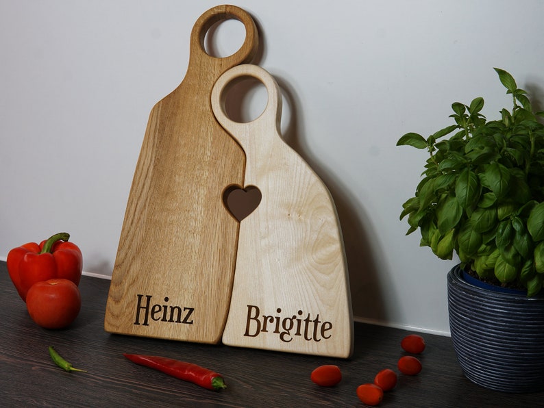May include: Two wooden cutting boards shaped like people, with a heart cutout where they touch. The boards are engraved with the names "Heinz" and "Brigitte".
