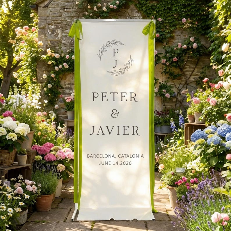 Pode incluir: Uma placa de casamento branca com fitas verdes e os nomes "Peter & Javier" em texto preto. A placa tamb&eacute;m inclui a localiza&ccedil;&atilde;o "Barcelona, ​​Catalunha" e a data "14 de junho de 2026". Uma coroa de flores com as iniciais "P J" est&aacute; no topo.