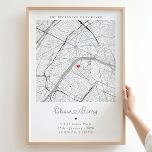 Könnte beinhalten: Gerahmter Kunstdruck einer Karte von Paris, Frankreich, mit einem roten Herzen, das einen Ort markiert. Der Druck enthält die Namen "Olivia & Henry", Datum und Koordinaten. Der Holzrahmen umgibt die schwarz-weiße Karte.