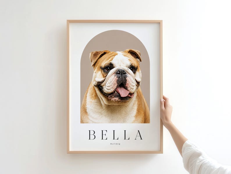 May include: A framed portrait print featuring a brown and white bulldog centered within a taupe arch graphic. Below the dog, the name BELLA is printed in black capital letters, followed by the word Bulldog in a smaller, simple font.
