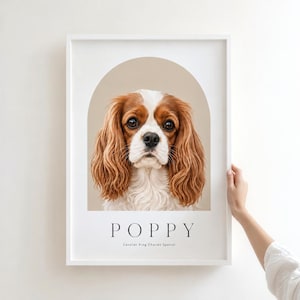 May include: A white framed wall art print featuring a portrait of a brown and white Cavalier King Charles Spaniel dog centered within a beige arch. The name POPPY is printed in black capital letters below the dog, with the text Cavalier King Charles Spaniel underneath.
