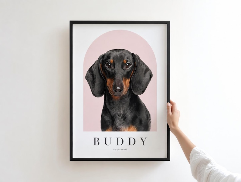 May include: A framed wall art print featuring a digital illustration of a black and tan dachshund dog centered within a soft pink arch. The name BUDDY is printed in black capital letters below the dog, followed by the word Dachshund.