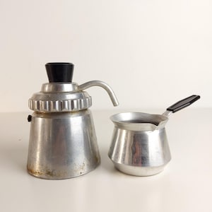 Peut inclure: Une cafetière italienne vintage en aluminium avec une poignée noire et une petite cafetière en aluminium avec une poignée noire. La cafetière italienne a un bouton noir et un bec verseur argenté.