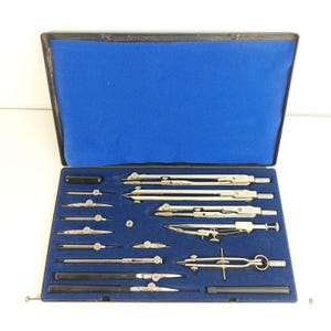 Peut inclure: Un coffret rectangulaire noir avec un intérieur en velours bleu contenant un ensemble de compas de dessin technique et d'instruments de précision en métal argenté. Le kit comprend divers diviseurs, rallonges et outils de géométrie.