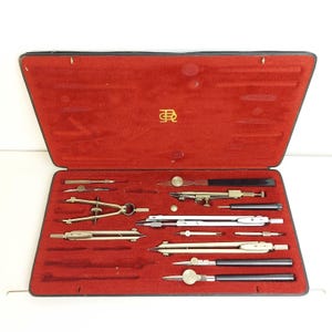 Peut inclure: Un ensemble de dessin vintage dans un étui noir avec un intérieur en velours rouge. L'ensemble comprend divers compas, diviseurs et autres outils de dessin, tous en métal. L'étui est ouvert, présentant les outils bien rangés.