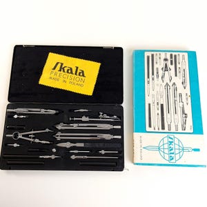 Könnte beinhalten: Ein Vintage-Zeichensatz in einem schwarzen Koffer mit dem Text "SKALA PRECISION MADE IN POLAND" auf einem gelben Etikett. Das Set enthält verschiedene silberfarbene Zirkel und Zeichenwerkzeuge. Eine blaue Box mit Illustrationen von Zeichenwerkzeugen ist ebenfalls vorhanden.