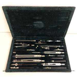 May include: An open, vintage drafting set in a dark green velvet-lined case. The set includes various silver and black drawing instruments, such as compasses, dividers, and pens, neatly arranged in individual slots. The case is rectangular with a hinged lid.