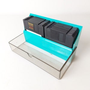 Könnte beinhalten: Ein türkisfarbenes Kunststoff-Aufbewahrungskoffer mit einem durchsichtigen Kunststoffdeckel, der einen Stapel schwarzer 3,5-Zoll-Disketten enthält. Die Disketten sind mit "Verbatim DataLifePlus 2HD High Density Diskettes" beschriftet.