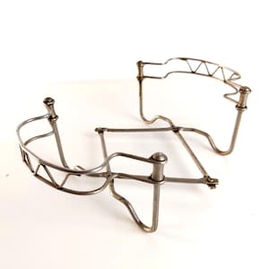 Könnte beinhalten: Zwei Vintage-Metall-Drahtrahmen, möglicherweise zum Halten von etwas. Die Rahmen sind silberfarben und haben ein geometrisches Design mit gebogenen und eckigen Elementen. Sie sind vor einem weißen Hintergrund platziert.