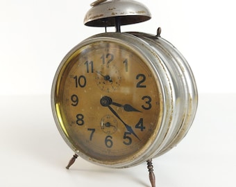 May include: A vintage silver alarm clock with a round face and black hands. The clock has a bell on top and stands on three legs.
