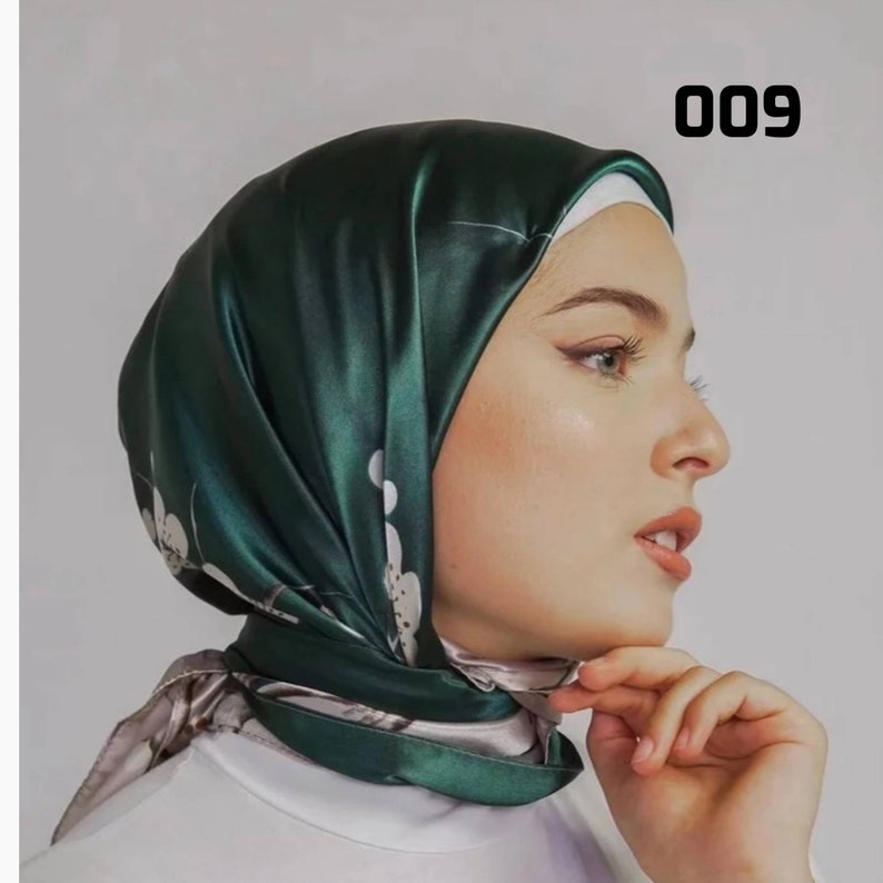 May include: A dark green satin headscarf with a floral pattern and the number "009" in the upper right corner. The scarf is draped over a person's head and shoulders, with the edges visible. The scarf has a shiny appearance.
