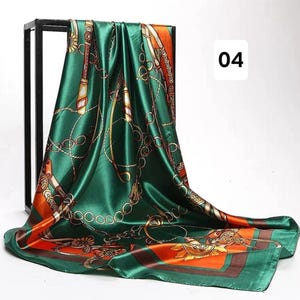 May include: A square, emerald green silk scarf with a gold chain and equestrian-themed pattern. The scarf has orange and brown borders and the number "04" in white. The scarf is draped over a black metal frame.