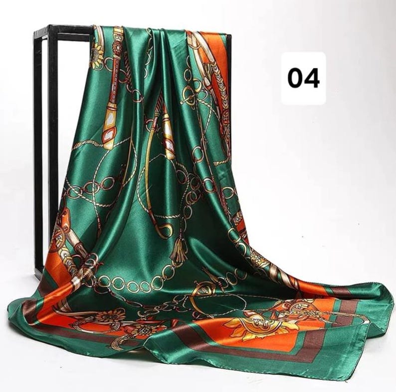 May include: A square, emerald green silk scarf with a gold chain and equestrian-themed pattern. The scarf has orange and brown borders and the number "04" in white. The scarf is draped over a black metal frame.