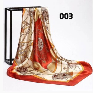 May include: A square silk scarf with an equestrian design. The scarf has a cream background with orange and brown details. The border is a solid orange, and the number "003" is printed on the scarf. The scarf is draped over a black stand.