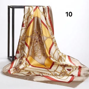 May include: A square silk scarf with a gold chain and buckle pattern on a cream background. The scarf has red and yellow accents and the number 10 in black in the upper right corner. The scarf is draped over a black metal stand.