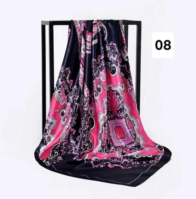 May include: A square silk scarf with a black border and a vibrant pink and black paisley design. The scarf is draped over a black metal stand, with the number "08" in a white box in the corner.