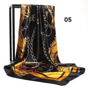 May include: Black and gold silk scarf with a chain and floral pattern. The scarf has a shiny finish and a contrasting gold border. The number "05" is visible in the upper right corner.