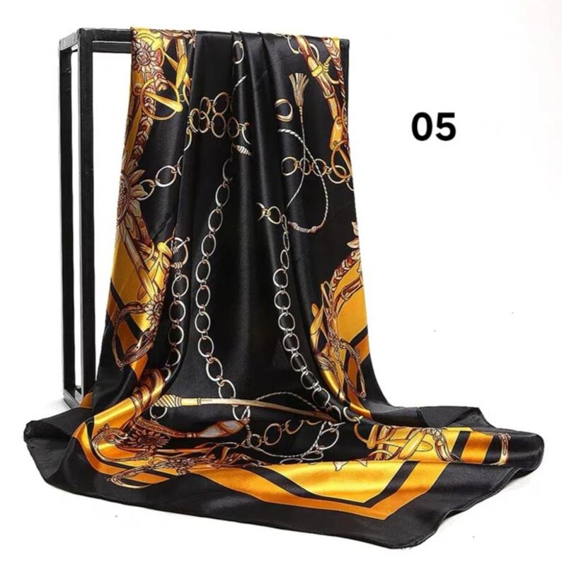 May include: Black and gold silk scarf with a chain and floral pattern. The scarf has a shiny finish and a contrasting gold border. The number "05" is visible in the upper right corner.