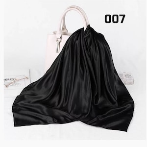 May include: A black satin scarf draped over a white handbag. The scarf has a glossy sheen and is folded to create soft, flowing lines. The number "007" is printed in black on the upper right corner. A pair of glasses and a perfume bottle are visible.