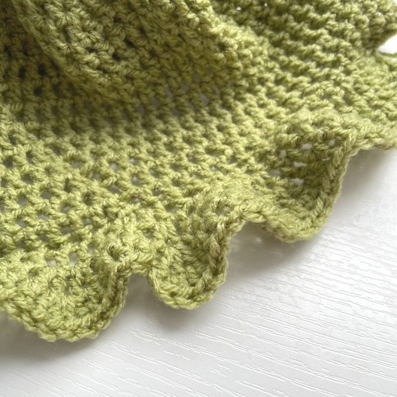May include: Close-up of a green crocheted fabric with a scalloped edge.