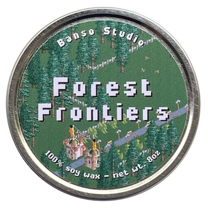May include: A round, silver tin lid with a green and white pixelated design. The lid features the text "Banjo Studio" and "Forest Frontiers" in white. The text "100% soy wax - net wt. 8 oz" is printed in white at the bottom of the lid.
