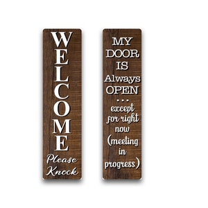 May include: Two wooden signs with white text. The left sign says "WELCOME Please Knock". The right sign says "MY DOOR IS Always OPEN... except for right now (meeting in progress)".