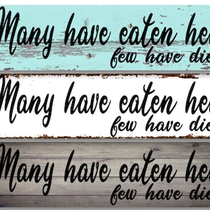 May include: Three wooden signs with a distressed paint finish. Each sign reads "Many have eaten here few have died". The signs are in different colors: light blue, white, and gray.