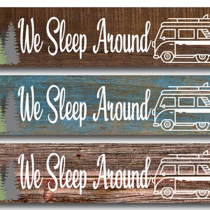 May include: Three wooden signs with a rustic wood grain background. Each sign features a white silhouette of a vintage camper van with a surfboard on top. The text "We Sleep Around" is written in white cursive font on each sign. The signs are in three different wood tones: brown, blue, and gray.