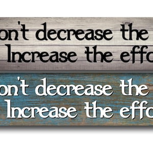 May include: Two rectangular wooden signs with motivational quotes. The top sign has a gray and brown wood grain background with black text that reads "Don't decrease the goal, Increase the effort." The bottom sign has a blue and brown wood grain background with white text.