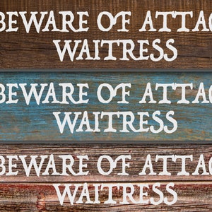 May include: Three rustic wooden signs with the text "BEWARE OF ATTACK WAITRESS" in white lettering. The signs have different wood grain patterns and colors, including brown, blue, and red.
