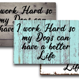 May include: Three wooden signs with a rustic look. The signs have the text "I work Hard so my Dogs can have a better Life" in black cursive font. The signs are in different colors: gray, blue, and white.