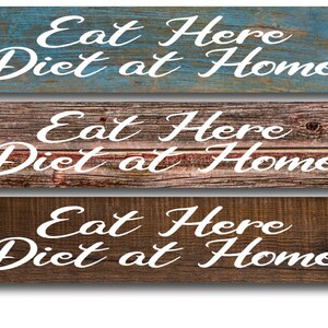 May include: Three rustic wooden signs with the text "Eat Here Diet at Home" in white cursive lettering. The signs have a distressed wood look with different shades of blue, brown, and gray.