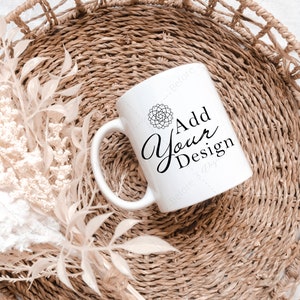 May include: White ceramic mug with a black design that says "Add Your Design". The mug is sitting in a woven basket with dried flowers.
