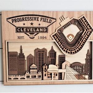 May include: A wooden wall art piece featuring a 3D model of Progressive Field, home of the Cleveland Guardians baseball team. The art piece includes the team's logo and the text "Progressive Field Cleveland EST. 1994".
