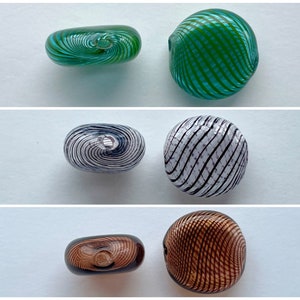 May include: Three glass beads with a swirl pattern. The beads are green, white with black swirls, and brown.