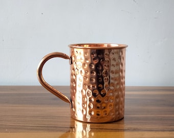 May include: A hammered copper mug with a handle. The mug has a shiny, metallic finish.