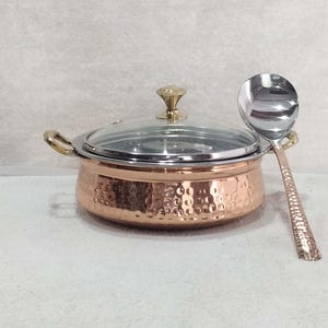 Puede incluir: Un plato de servir de cobre con un acabado martillado y una tapa de vidrio. El plato viene con una cuchara de servir a juego.