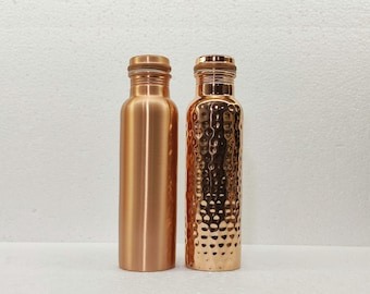 May include: Two copper water bottles. One bottle is smooth, the other has a textured, hammered design. Both bottles have a matching copper cap. The bottles are cylindrical and have a shiny, metallic finish. The background is a plain white.