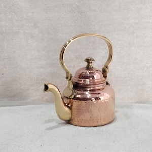 May include: A small, copper-colored teapot with a hammered texture. It features a gold-colored handle, spout, and accents. The teapot has a rounded body and a lid with a small knob. A decorative item.