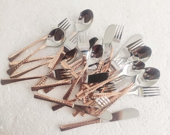 May include: A set of silverware with a mix of silver and copper-toned utensils. The utensils include spoons, forks, and knives. The silverware has a hammered texture.