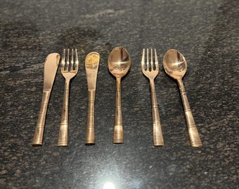 May include: A set of six antique gold-colored flatware pieces, including forks, spoons, and butter knives. The utensils are arranged on a dark, speckled surface, showcasing their vintage design and polished finish. Ideal for a vintage-themed dining setting.
