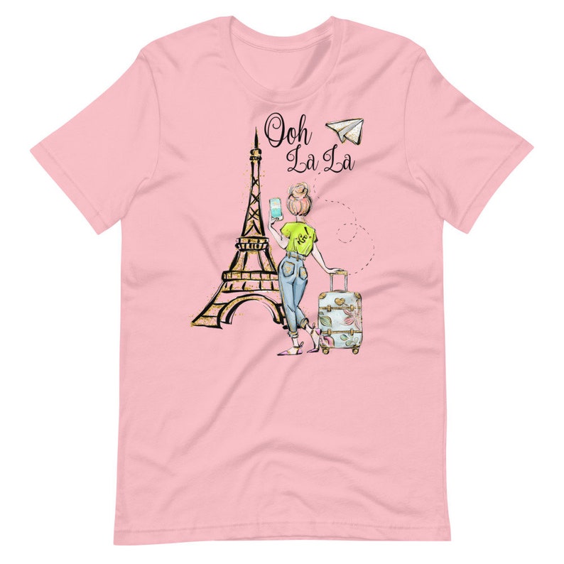 Op de afbeelding: Roze T-shirt met een afbeelding van de Eiffeltoren, een vrouw met een koffer en de tekst "Ooh La La" met een papieren vliegtuig.